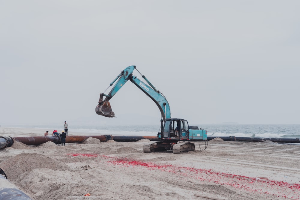 blue and black excavator on brown sand near body of water during daytime