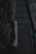 A close-up view of a backpack with visible padded sections and adjustable straps. There is a black cylindrical object attached to the strap, which appears to be a small flashlight.