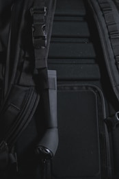 A close-up view of a backpack with visible padded sections and adjustable straps. There is a black cylindrical object attached to the strap, which appears to be a small flashlight.