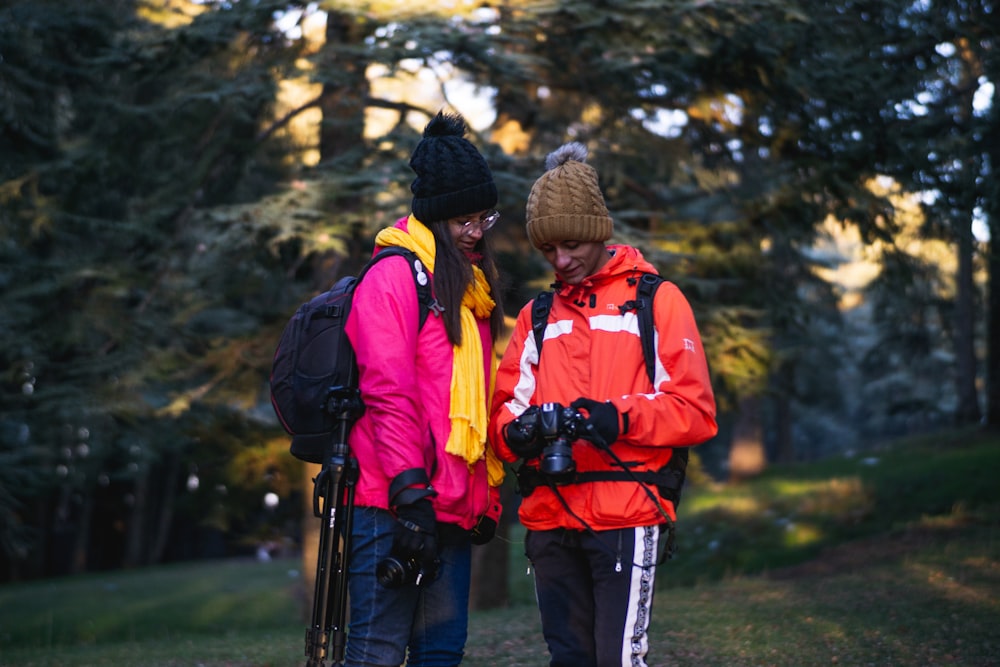 2 person wearing red and black jacket and black knit cap standing on green grass field