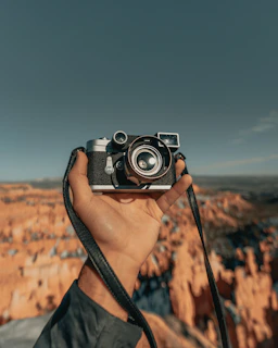 A close-up of a traveler’s hand holding a vintage camera, capturing a scenic landscape.