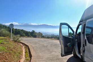 A spacious tempo traveller parked beside a scenic hill station road with misty mountains in the background.
