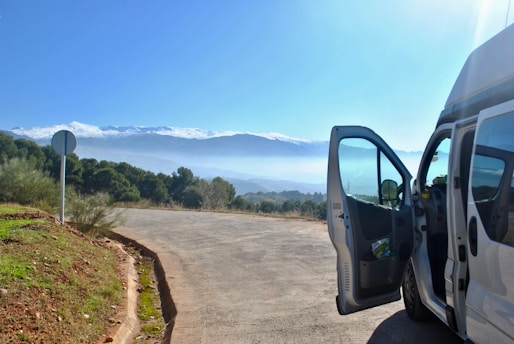 A clean, modern van parked near a scenic Catskills mountain road under a clear blue sky.