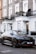 A sleek, black luxury SUV is parked on a street with elegant, brick townhouses in the background. The vehicle's design is modern and sporty, with tinted windows and distinctive branding. The backdrop features white-trimmed windows and ornate wrought-iron balconies adorned with potted plants.