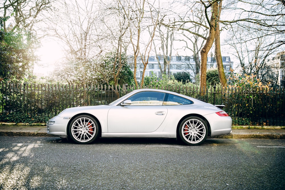 white coupe parked on gray concrete pavement near bare trees during daytime