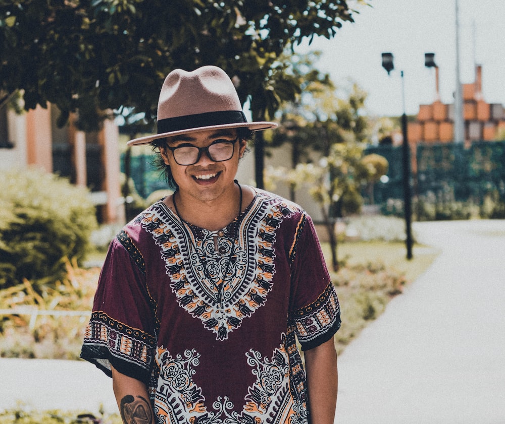 woman in red and white floral shirt wearing brown fedora hat standing on road during daytime