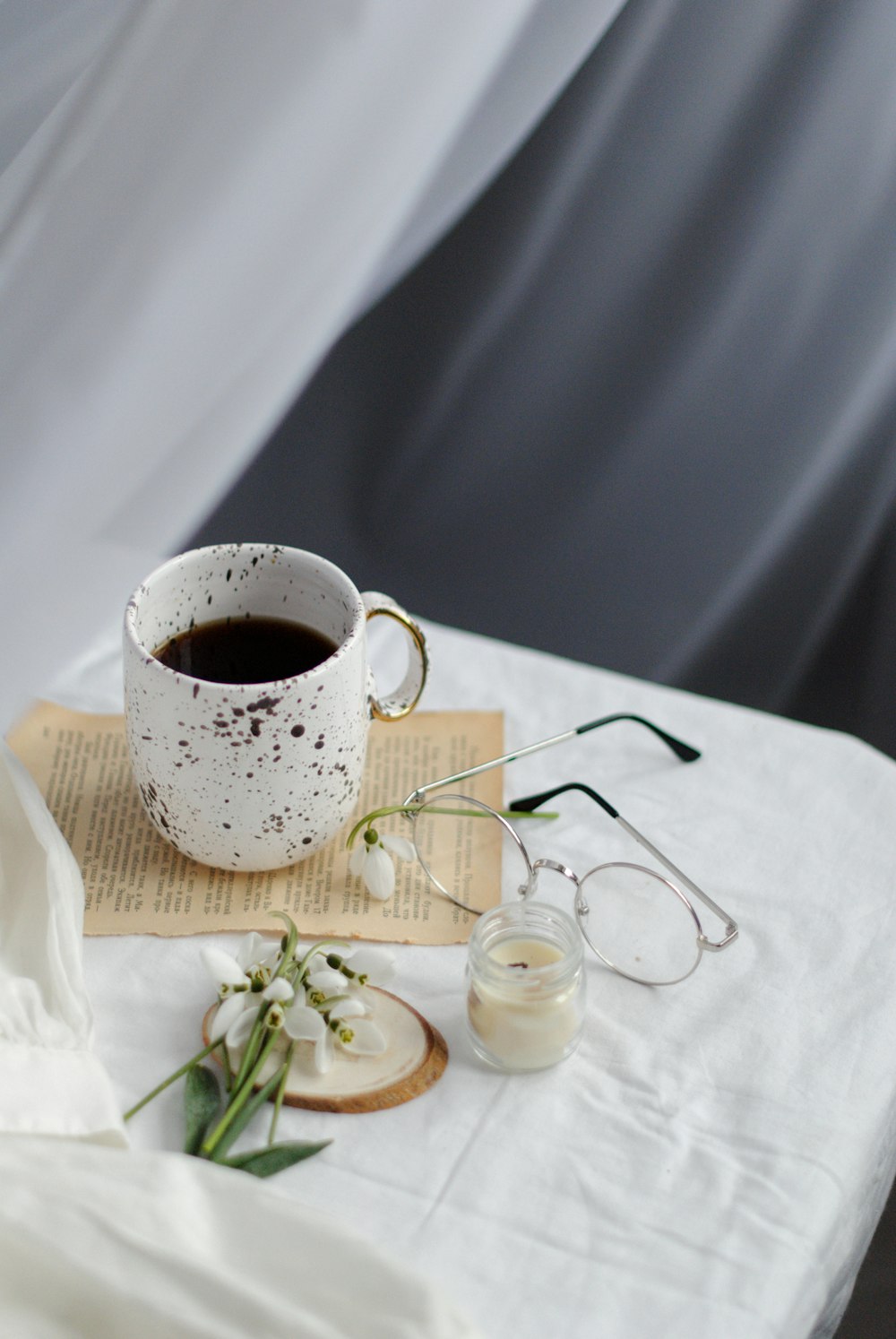 white ceramic mug on white textile beside eyeglasses