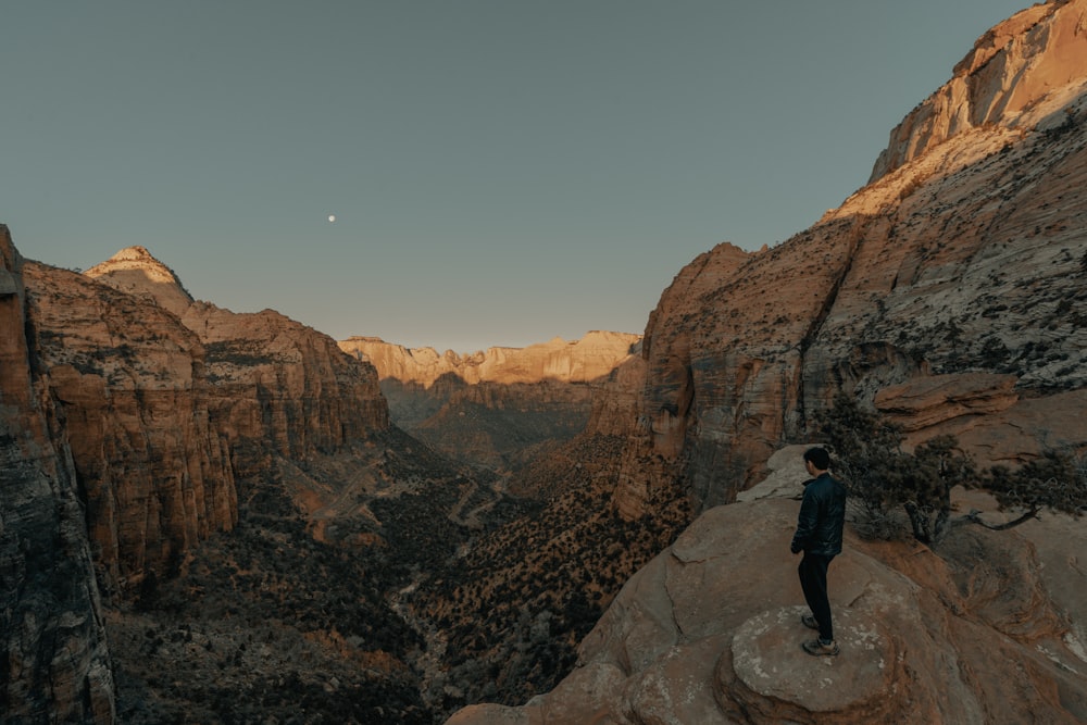 man in black jacket standing on rock formation during daytime