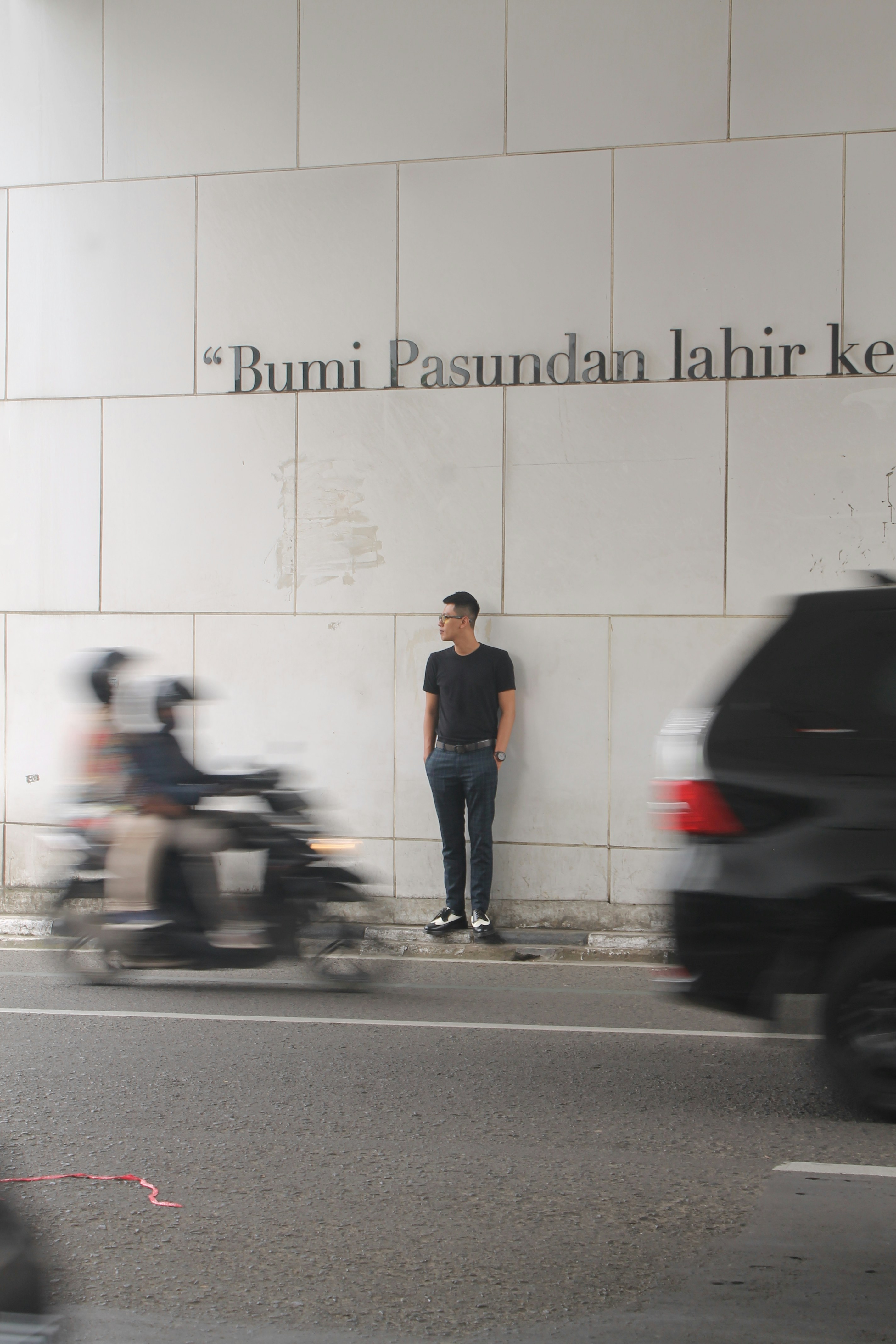 Pria dengan T-shirt biru dan jeans denim biru berdiri di samping sepeda motor hitam