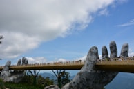 Golden Bridge held by giant stone hands at Ba Na Hills under a bright blue sky.