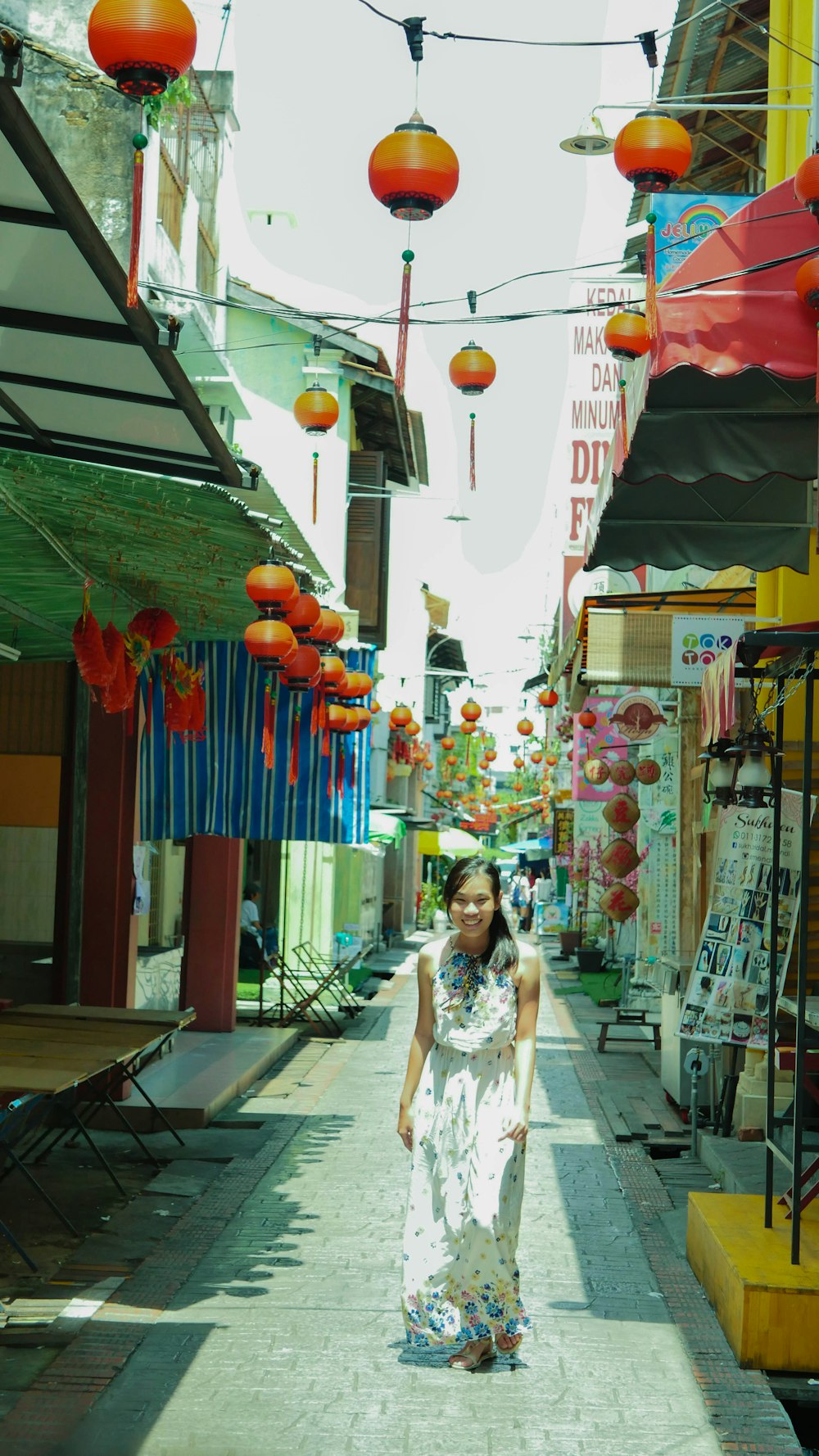 woman in white and pink floral dress standing near red and yellow balloons