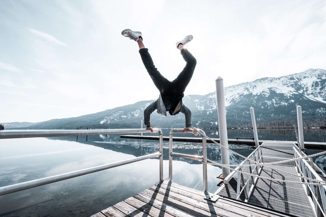 woman in black long sleeve shirt and black pants jumping on brown wooden dock during daytime