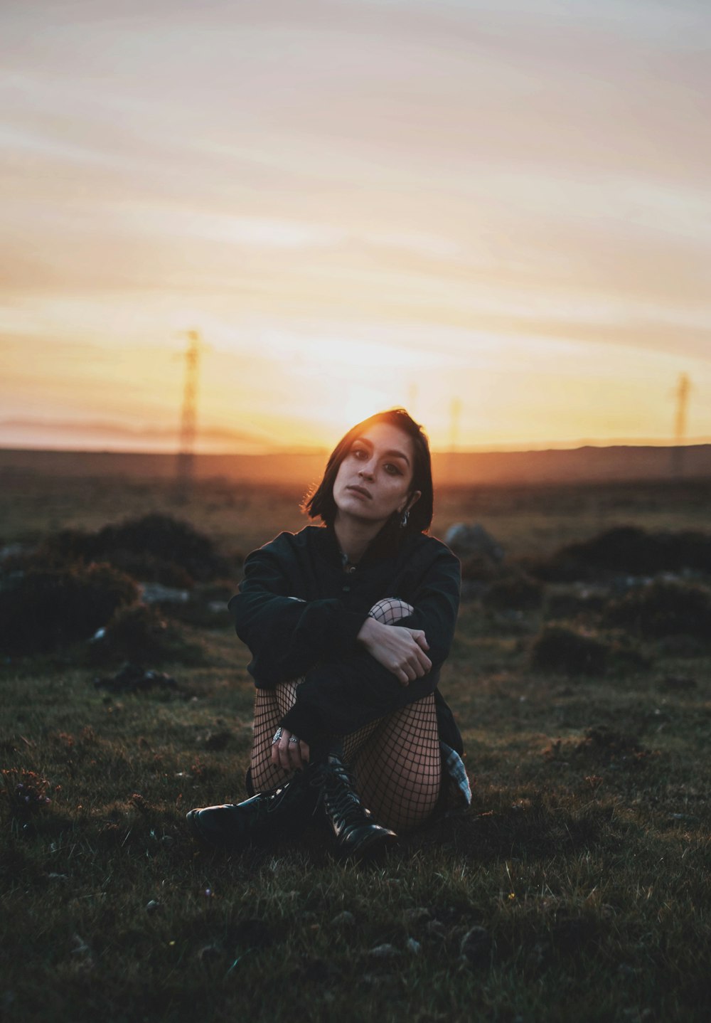 woman in black jacket sitting on grass field during sunset