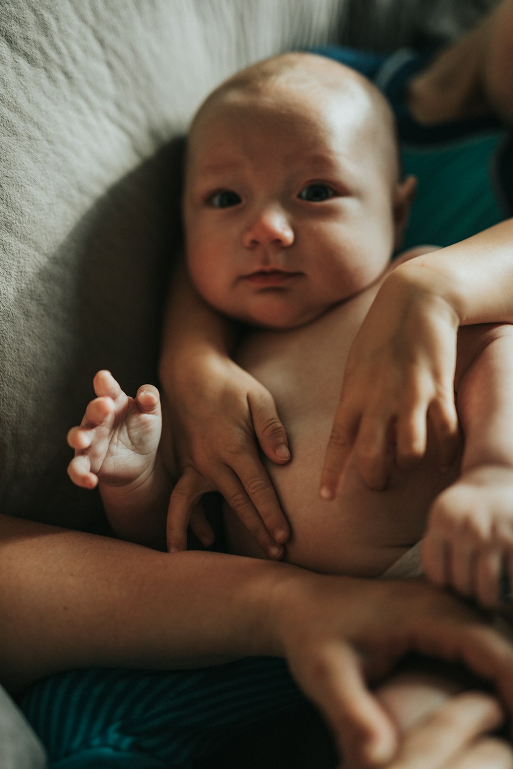 topless baby lying on gray textile