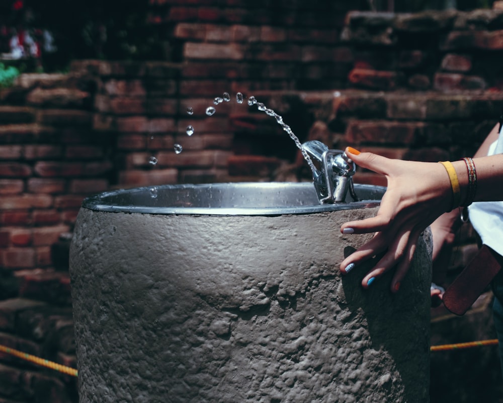 person pouring water on black round container