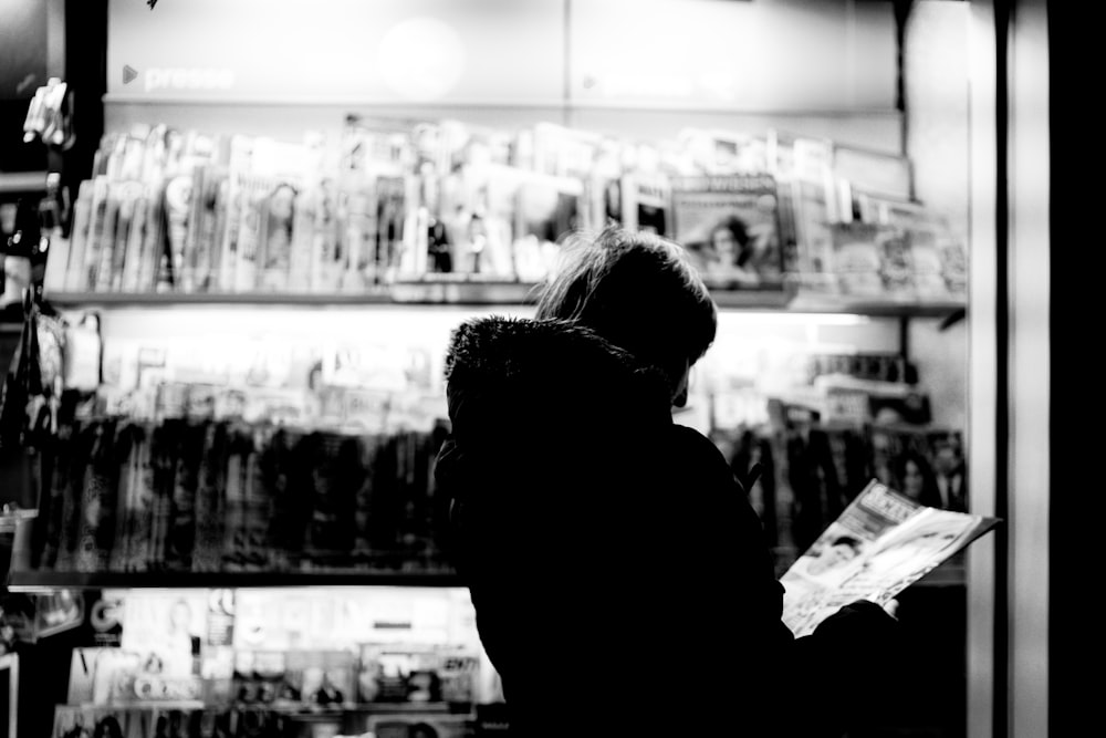 grayscale photo of person in black jacket standing in front of store