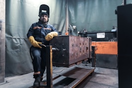 man in black helmet and brown jacket sitting on brown wooden box