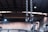 Heavy metal chains with large hooks dangle from the ceiling of an industrial building, with a blurred background showing the high roof structure and metal beams of the interior.