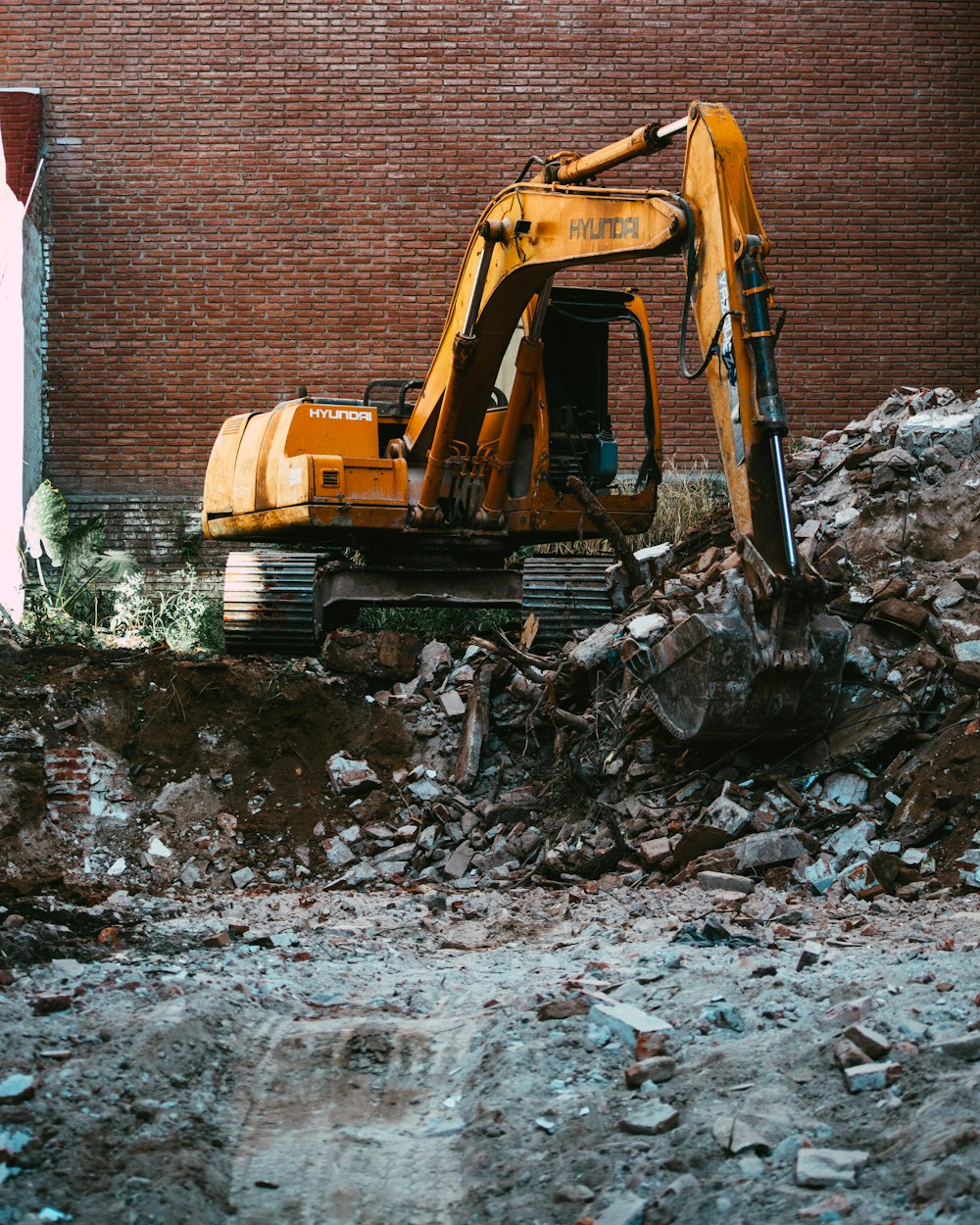 yellow excavator beside brown brick wall