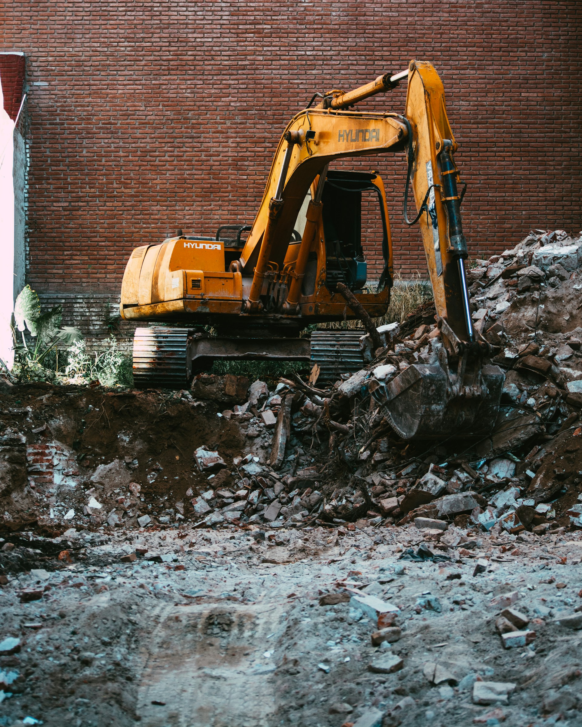 yellow excavator beside brown brick wall