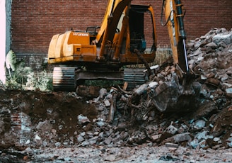 yellow excavator beside brown brick wall