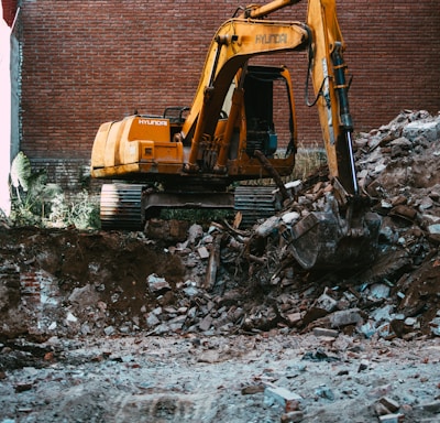 yellow excavator beside brown brick wall