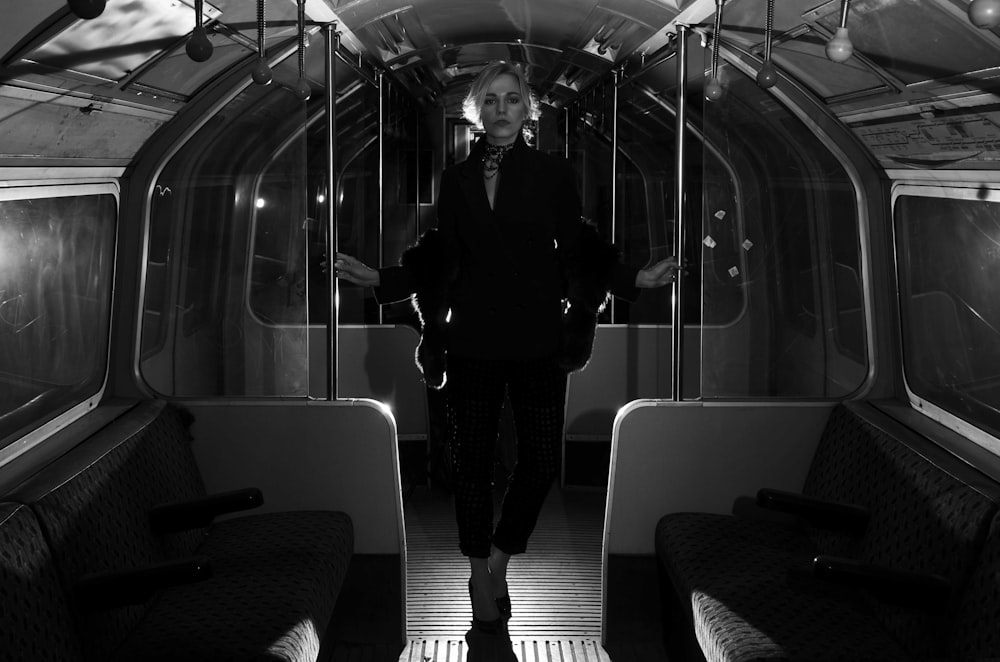 grayscale photo of woman in black coat and pants standing on train