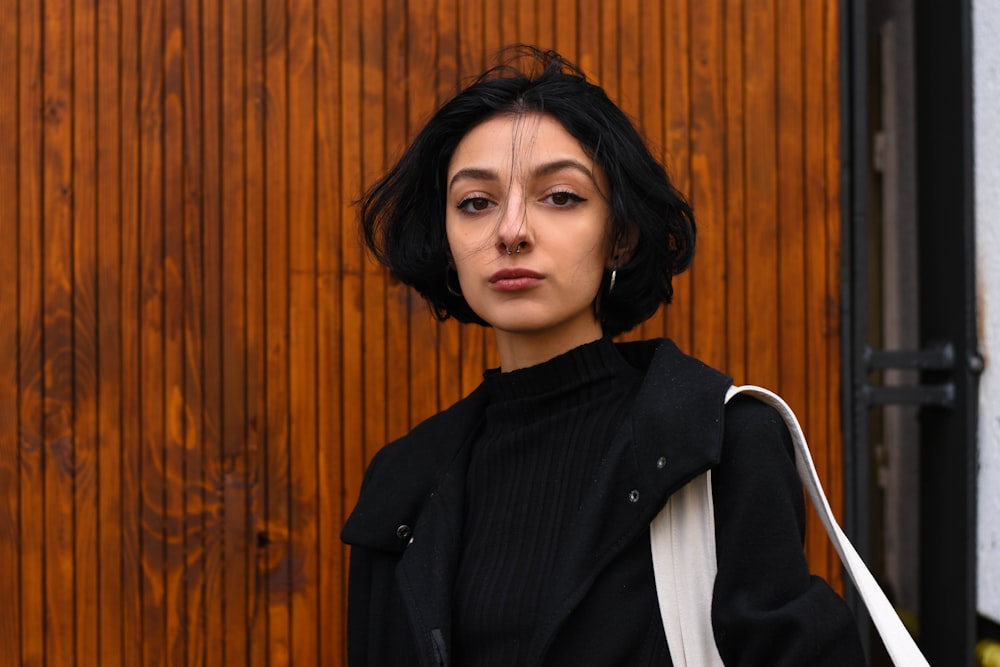 woman in black blazer standing near brown wooden wall