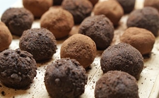 Chocolate truffles are arranged in a close-up view on a wooden surface. Some truffles are coated in cocoa powder while others have a darker, crumbly chocolate coating.