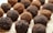 Chocolate truffles are arranged in a close-up view on a wooden surface. Some truffles are coated in cocoa powder while others have a darker, crumbly chocolate coating.