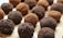 Chocolate truffles are arranged in a close-up view on a wooden surface. Some truffles are coated in cocoa powder while others have a darker, crumbly chocolate coating.
