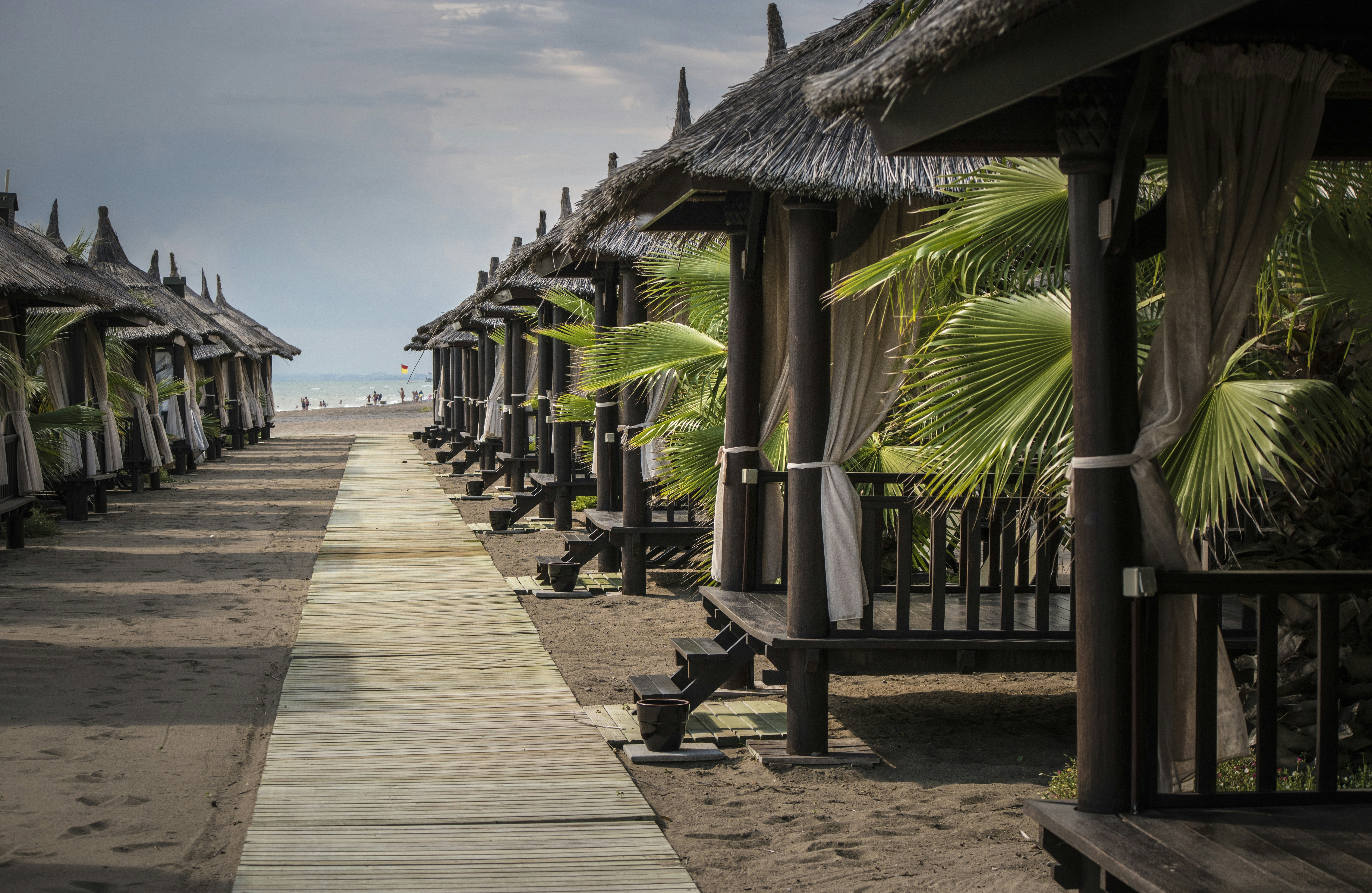 brown wooden pathway with green banana trees on side, beach houses somewhere in Turkey.