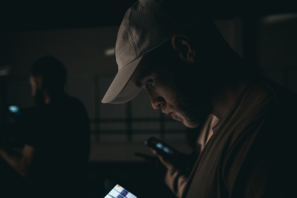 homme en chemise noire et casquette blanche tenant un smartphone