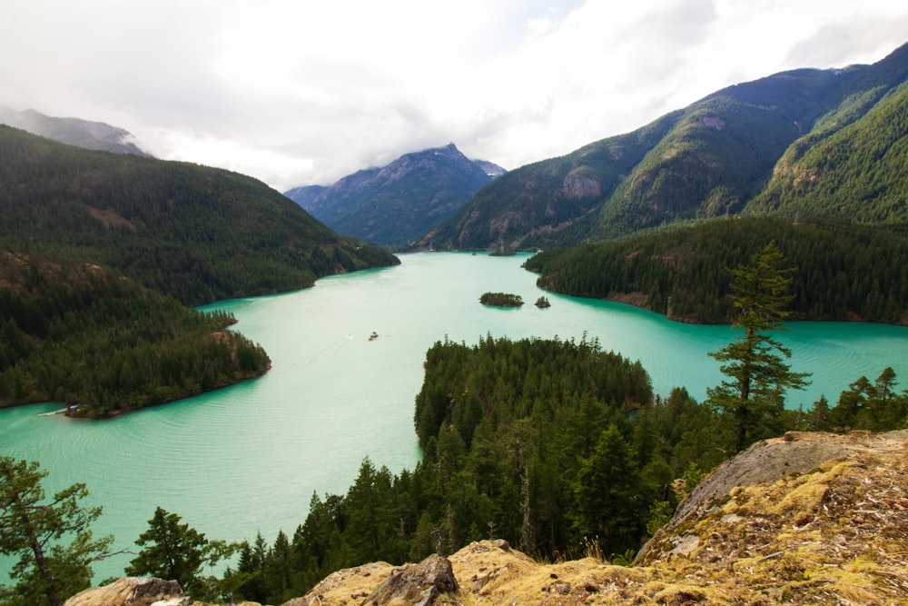 green lake surrounded by green trees and mountains during daytime