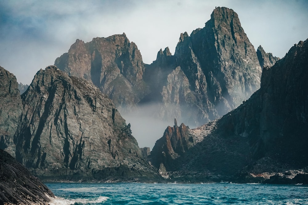 montanha rochosa marrom ao lado do mar azul sob o céu branco durante o dia