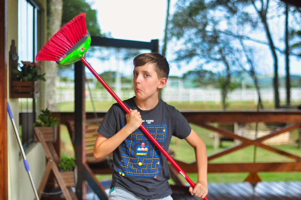 menino na camiseta cinza do pescoço da tripulação segurando o bastão verde e vermelho