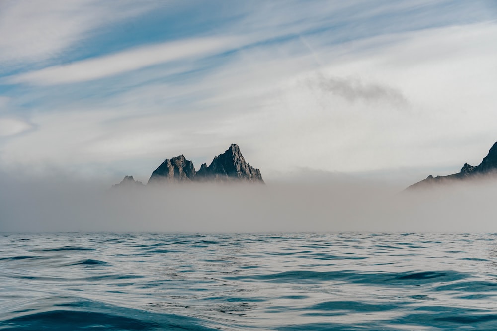 body of water near mountain under white clouds during daytime