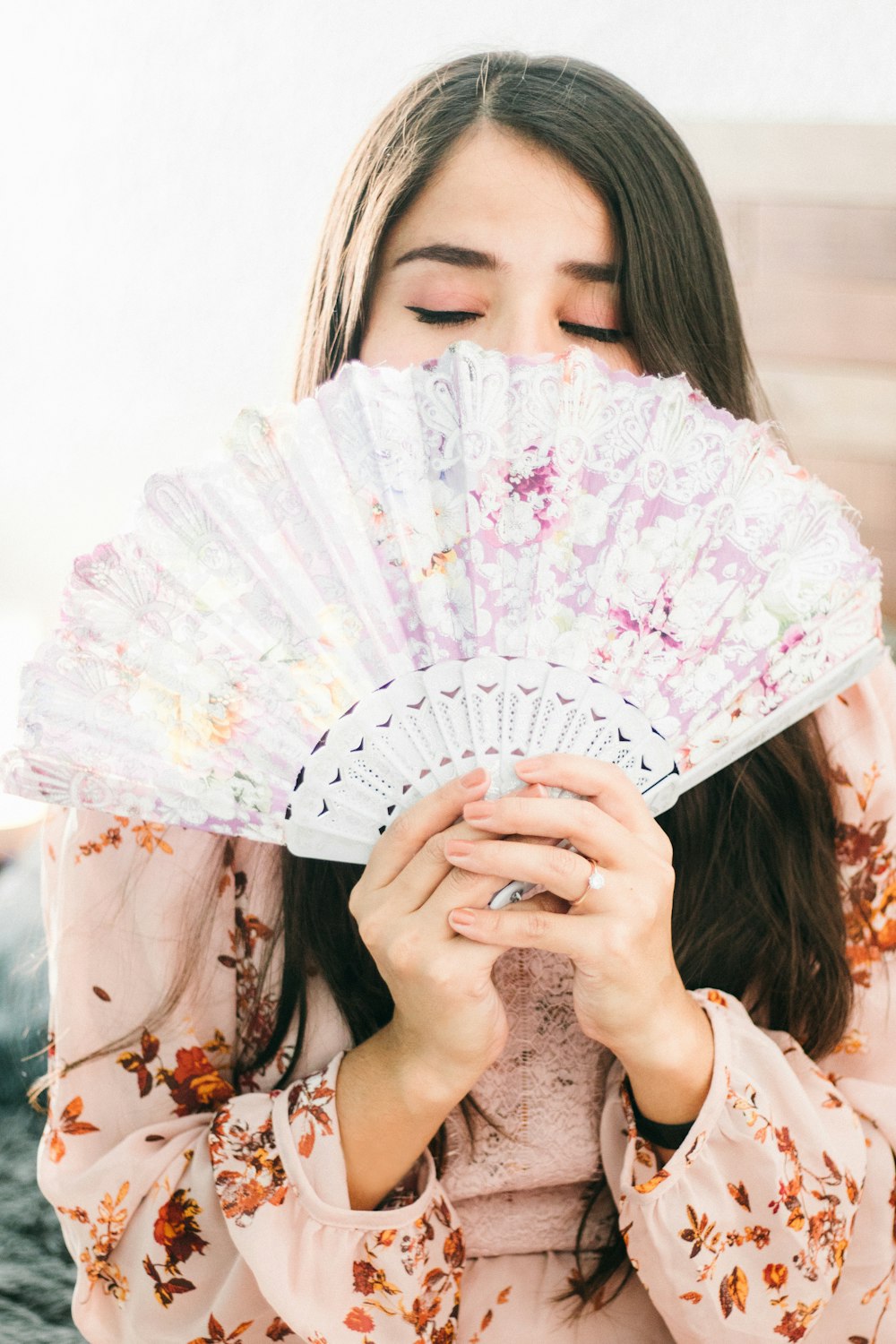 woman covering her face with white floral hand fan
