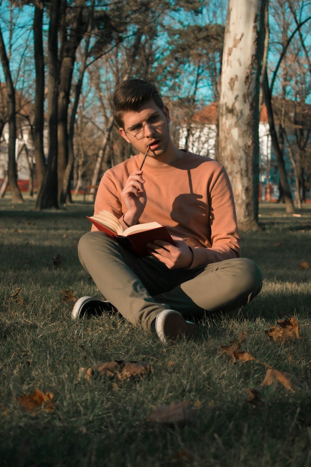 man in brown long sleeve shirt sitting on green grass field reading book during daytime