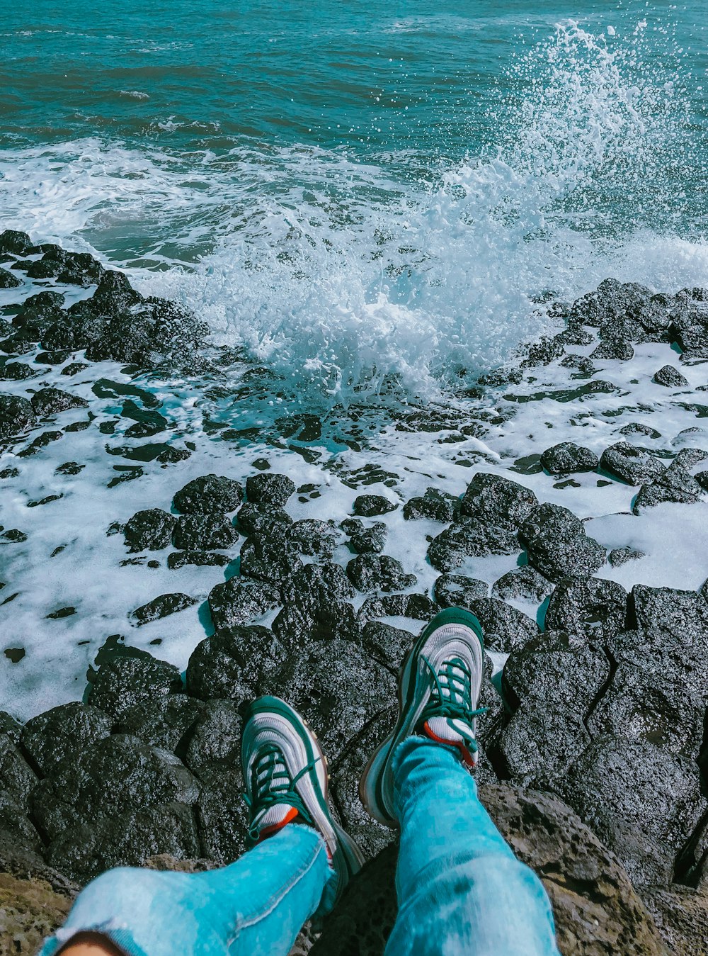 person in green and white sneakers standing on rocky shore during daytime