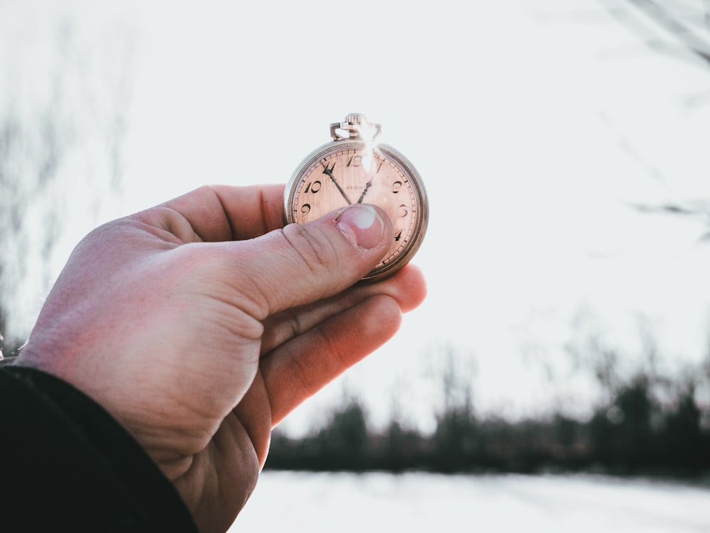 Persona sosteniendo un reloj de bolsillo plateado