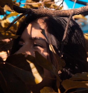 A softly lit photograph capturing a solitary figure framed by dappled sunlight filtering through leaves.