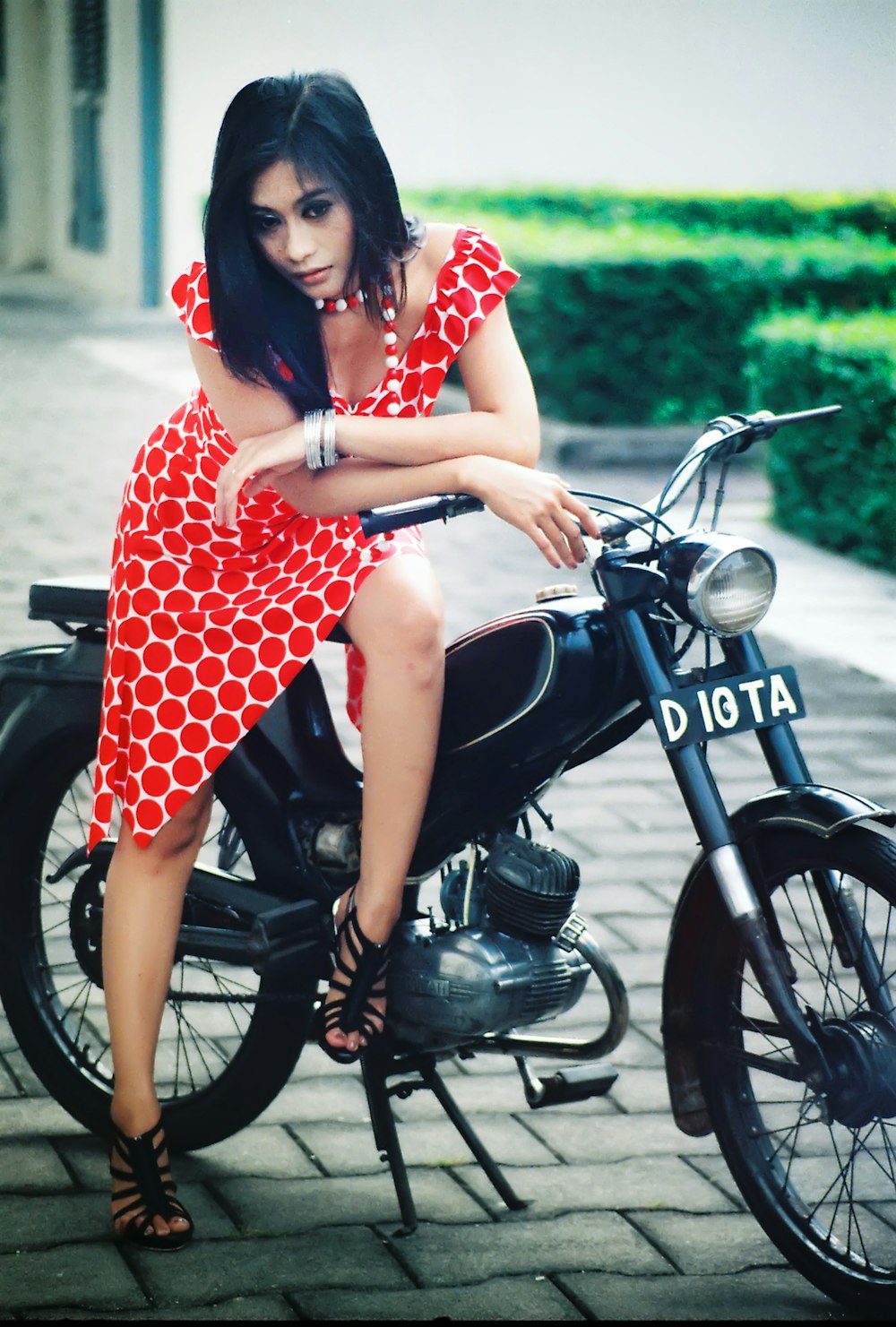 Donna in abito a pois rosso e bianco che cavalca su una moto nera