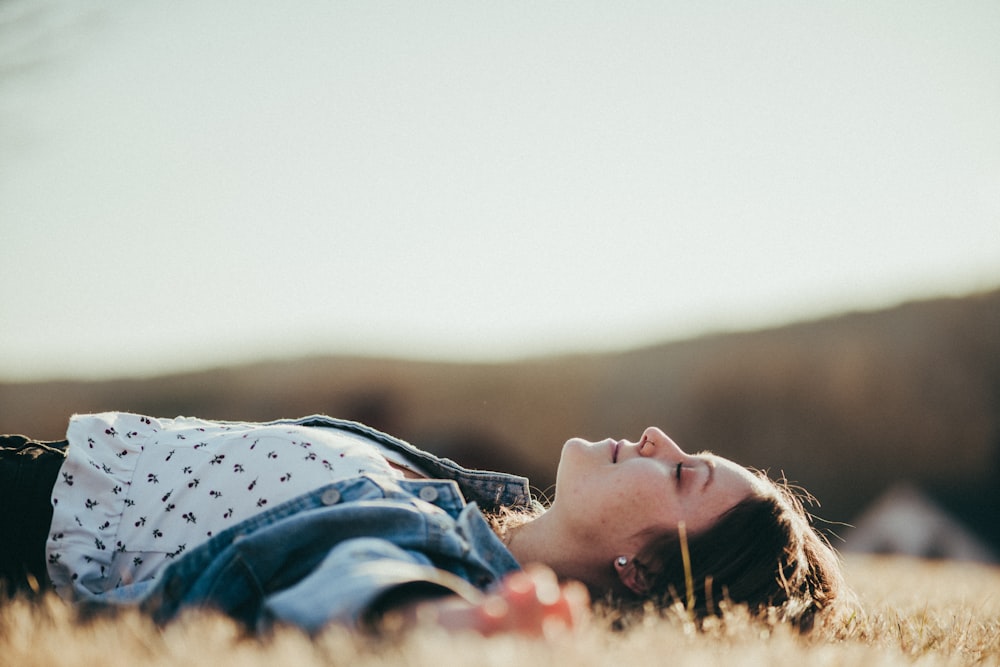 woman in blue and white polka dot shirt lying on brown grass field during daytime