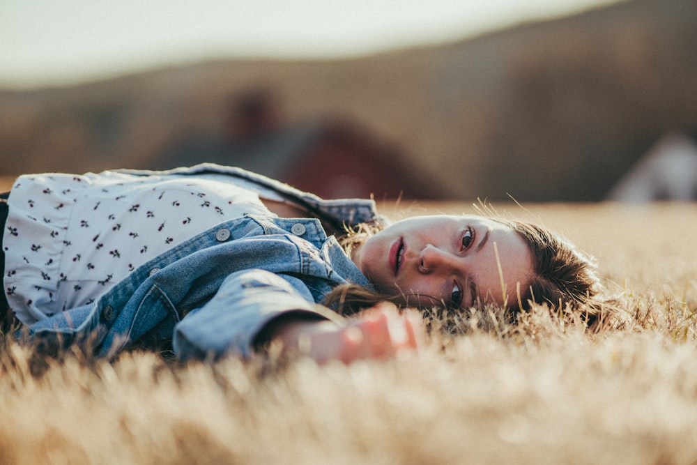 boy in blue denim jacket lying on brown grass field during daytime