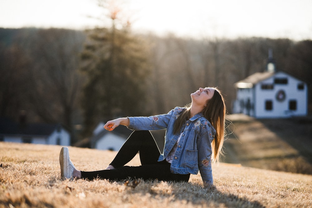 woman in blue denim jacket sitting on brown grass during daytime