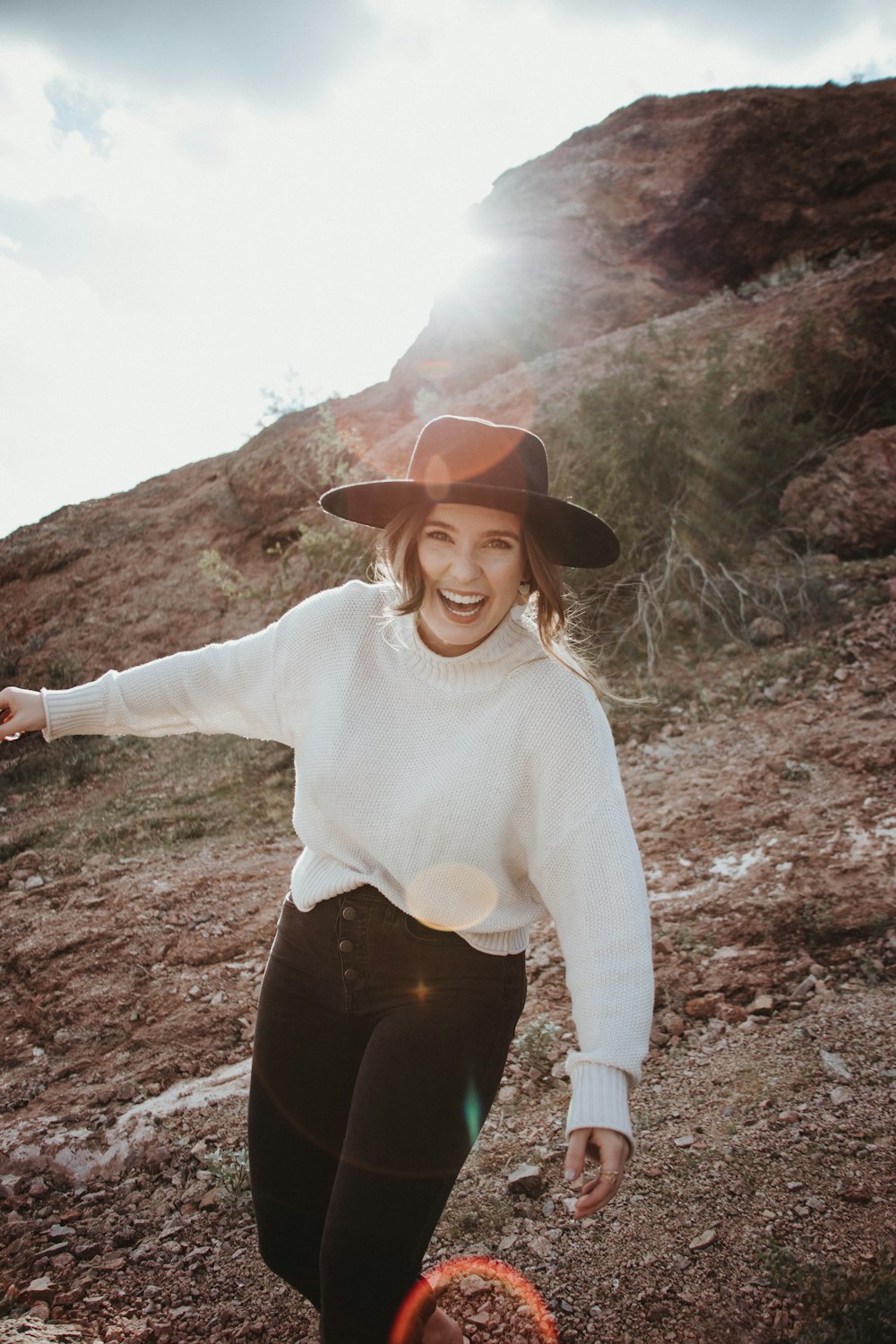 Femme en pull blanc et pantalon noir debout sur un sol brun pendant la journée