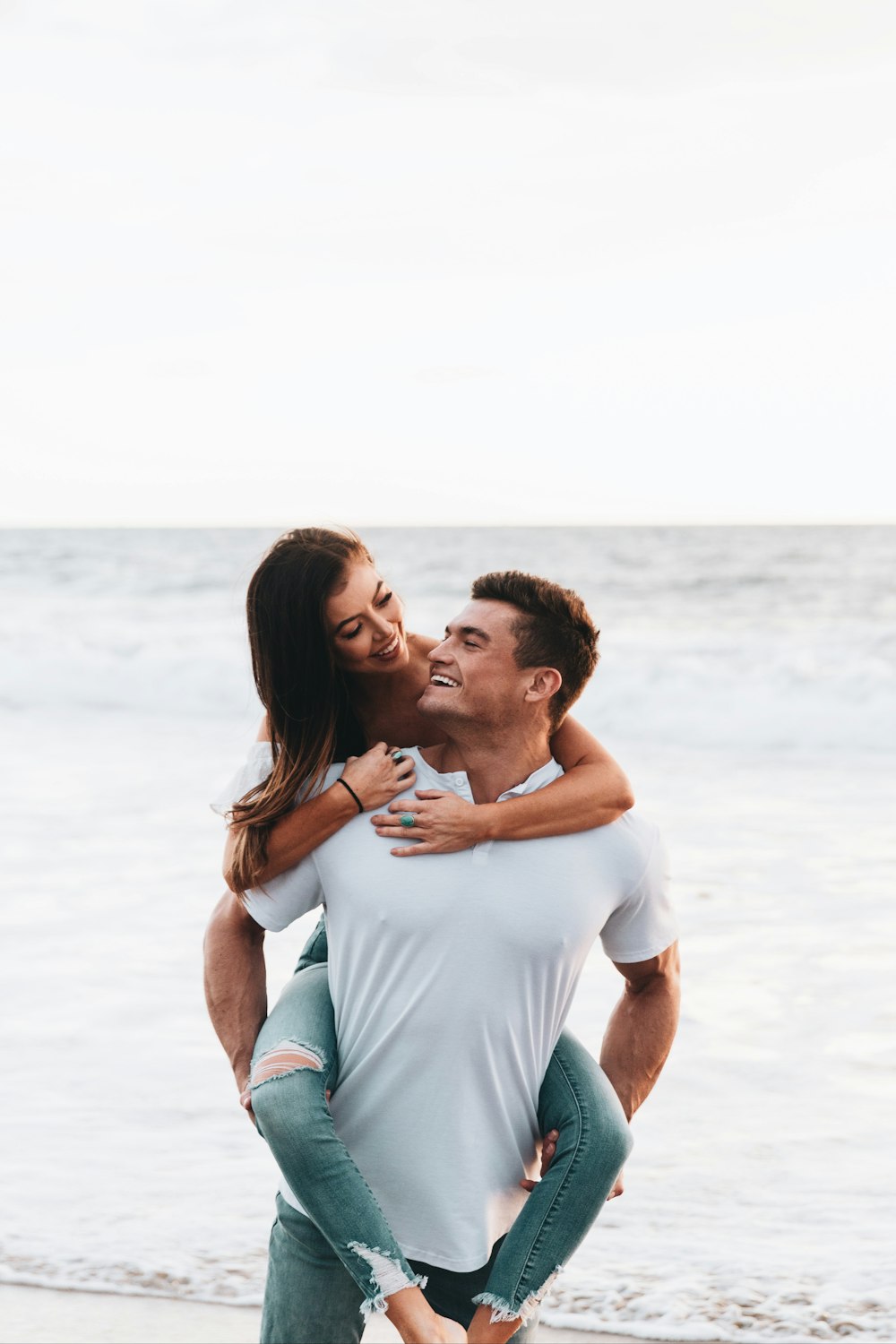 Mann im weißen T-Shirt küsst tagsüber Frau in weißem Tanktop am Strand