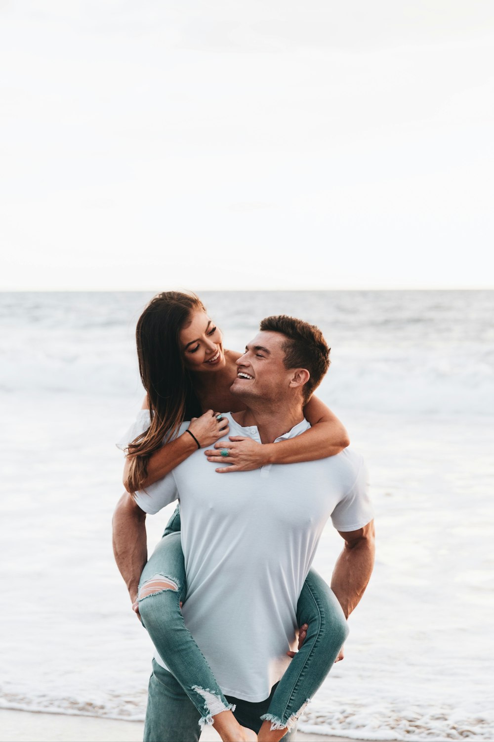 man in white t-shirt kissing woman in white tank top on beach during daytime