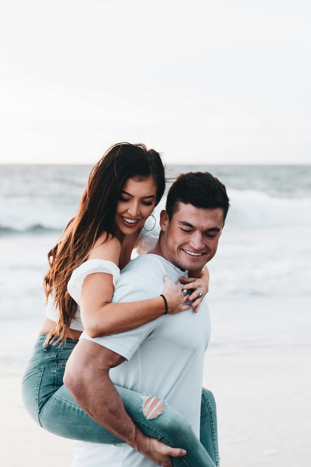 man in white shirt hugging woman in white shirt on beach during daytime